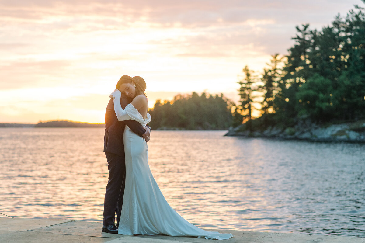 Bride and groom embrace at sunset on the dock in Muskoka