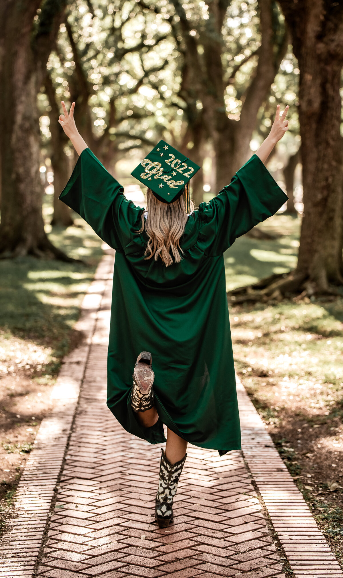 A senior wearing a green cap and gown holding her fingers in the air to read "22".