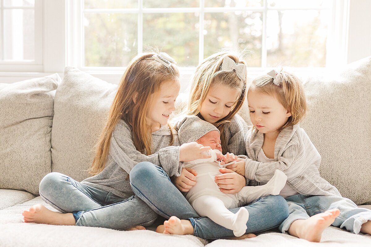 three sisters hold baby brother  during in home newborn photo session with Sara Sniderman Photography in Sherborn Massachusetts