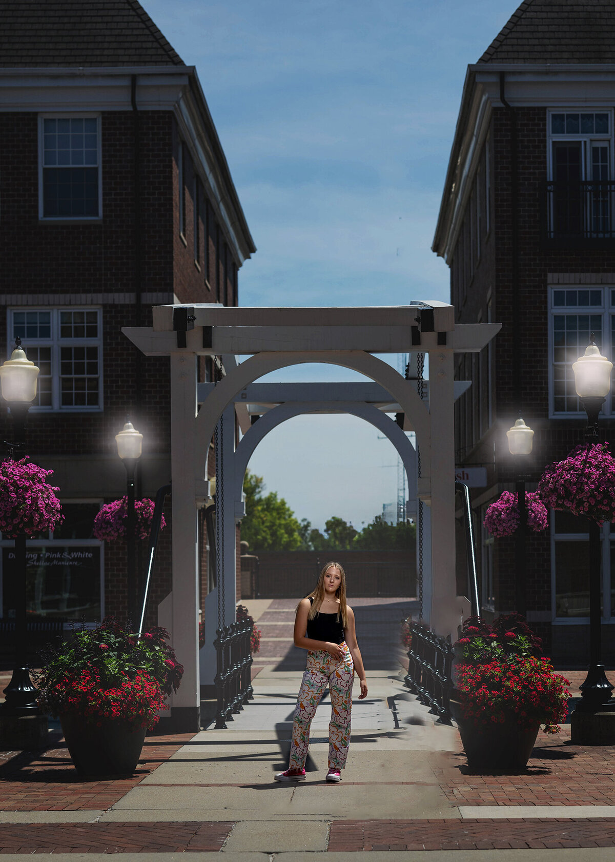 A high school senior stands on a bridge with a pergola in colorful pants