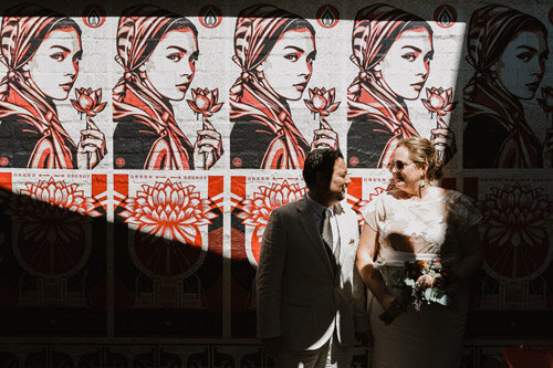 A wedding photograph from a Sydney Elopement in Chippendale. Walking the backstreets and exploring for interesting and unique imagery. The couple stands in front of a mural in direct sunlight.