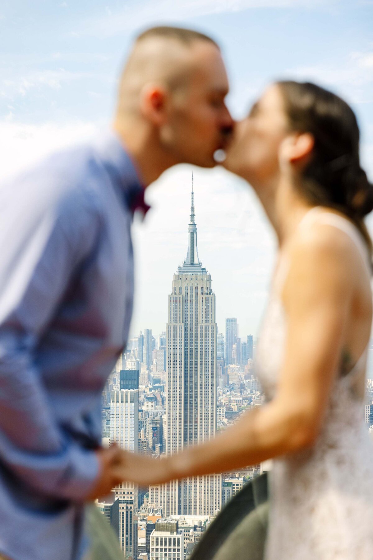 A couple kissing with the empire state building between them in the distance.