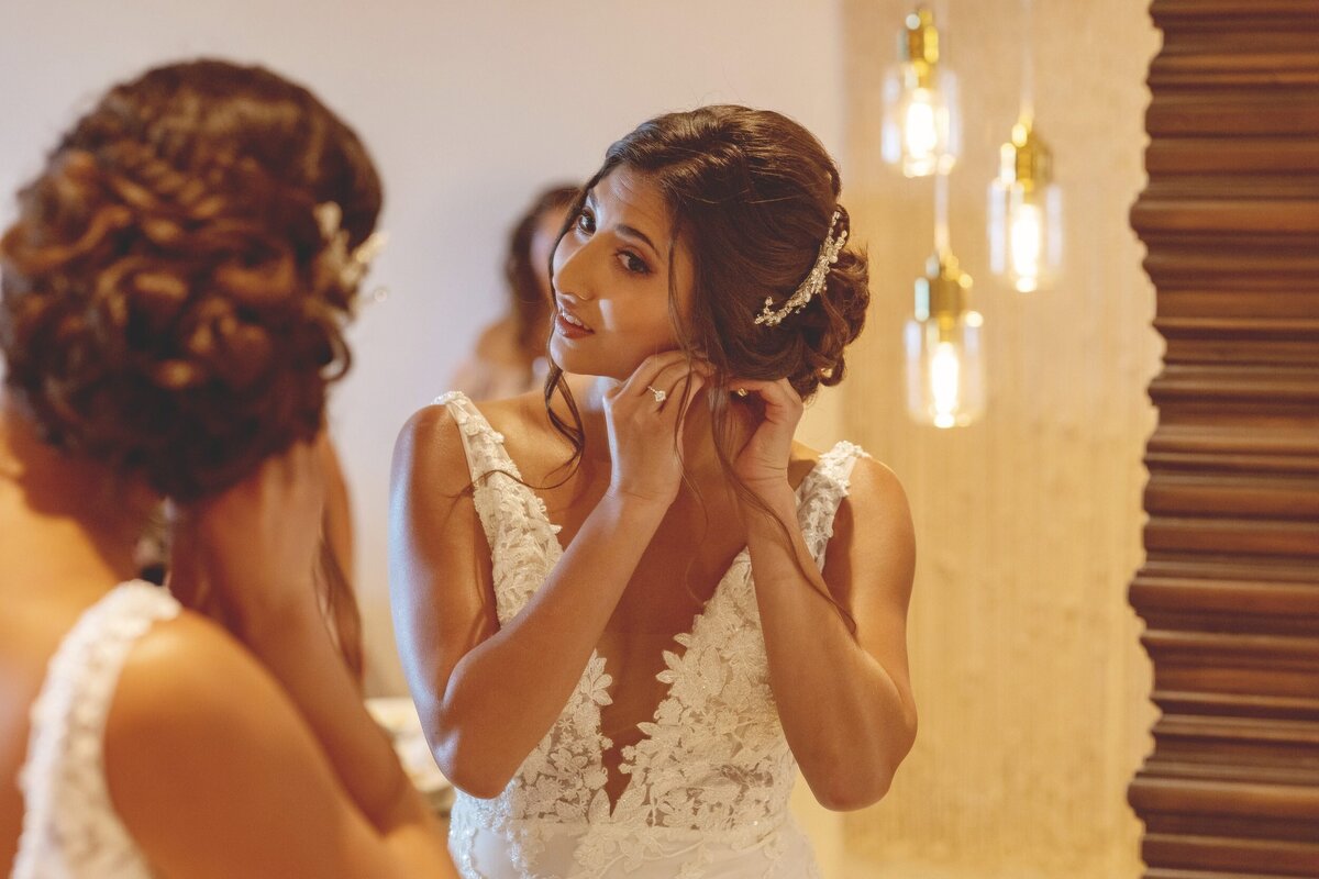 Bride putting on ear ring in mirror at Secrets Maroma Riviera Maya.