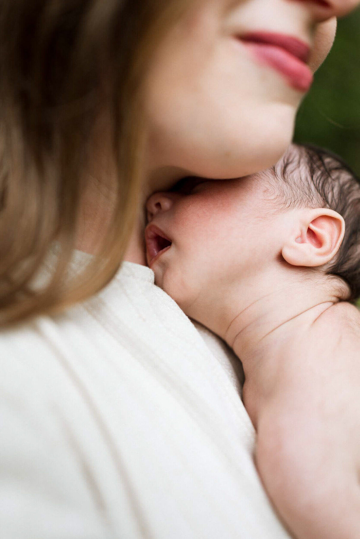Close-up of a newborn resting peacefully against their mother's chest. Captured with artistic focus on the intimacy of the bond.