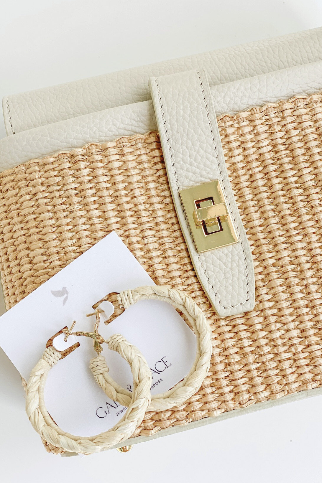 Natural woven hoop earrings, displayed on Gaby & Grace branded card next to a cream leather and straw clutch.