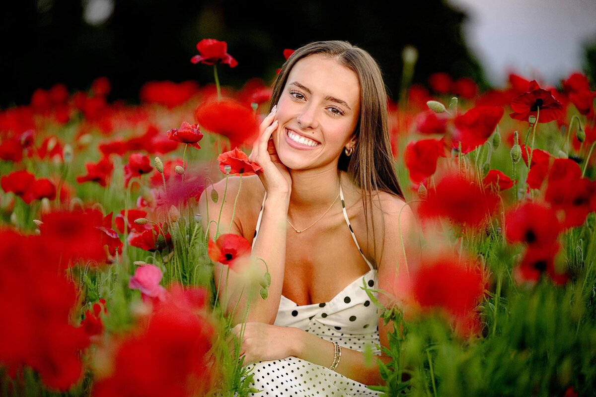 Surrounded by the red poppy blooms at blue hill gardens in monroe,nc this senior wearing a black and white dress smiles during her senior photos