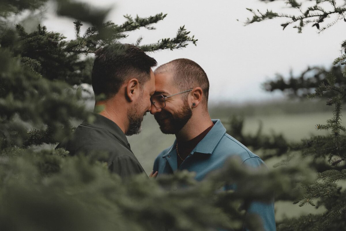 LGBTQ Couple leaning foreheads in front of trees