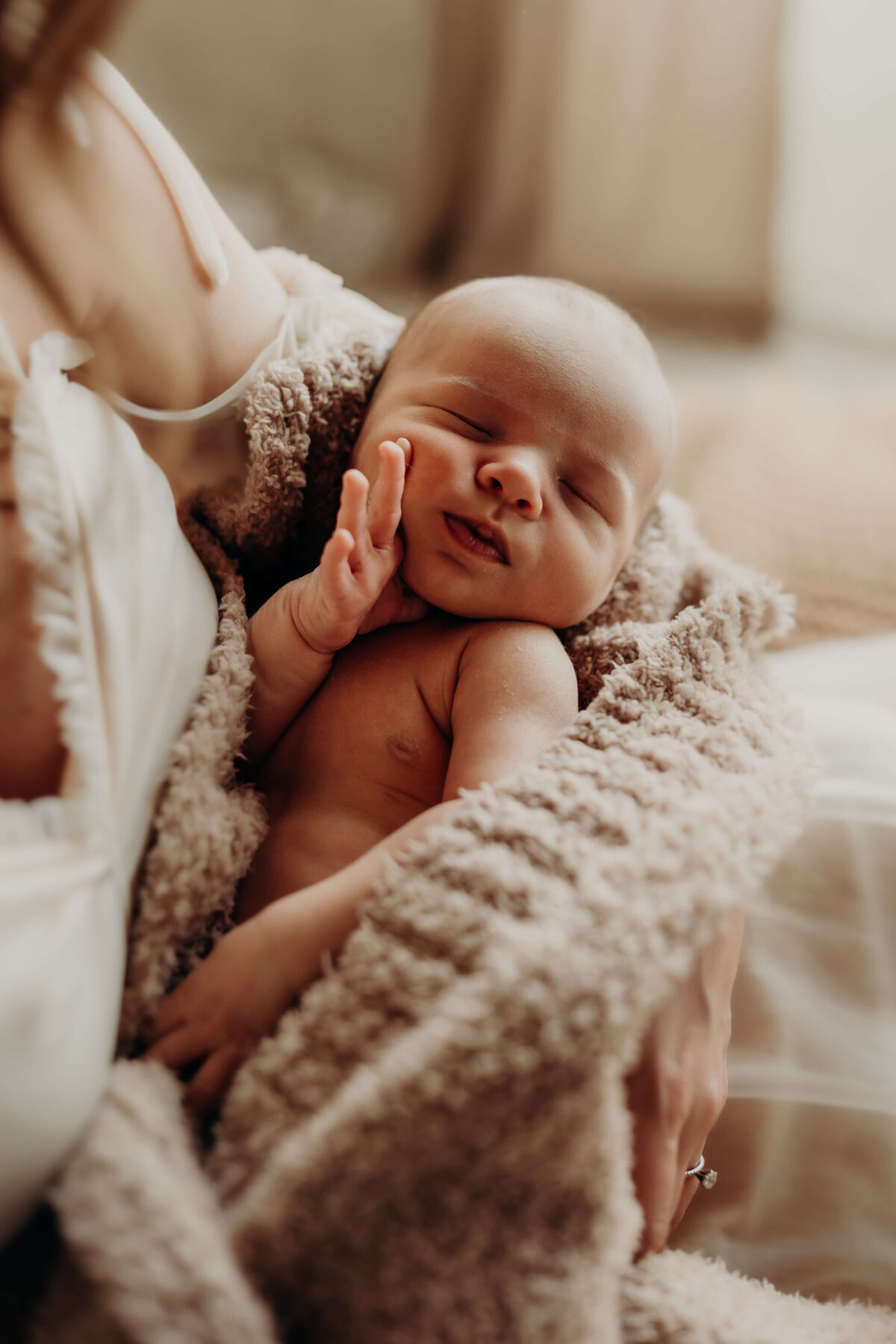 infant boy touches his face while wrapped in a luxe blanket
