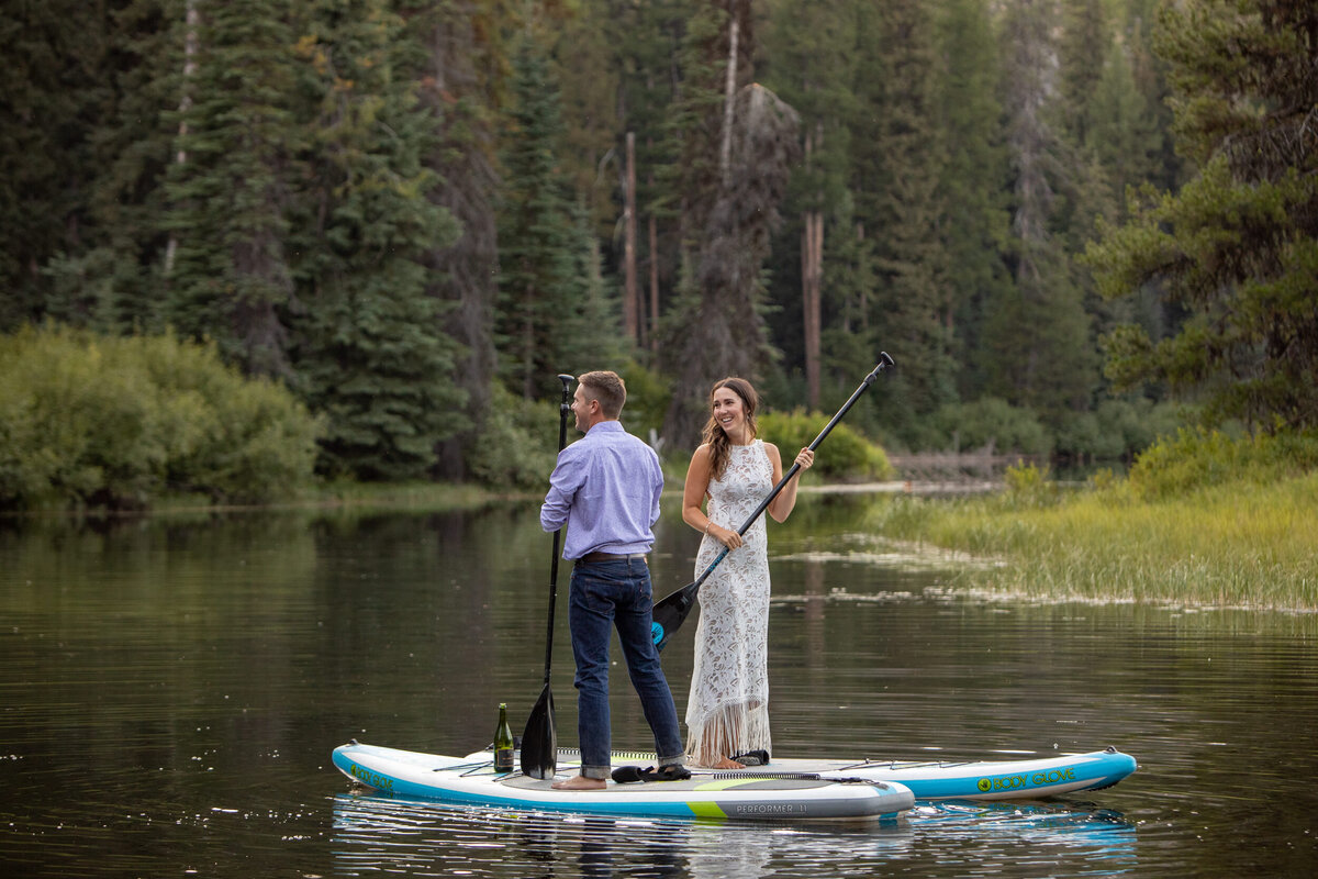 A bride and groom paddle board on a lake in Idaho.