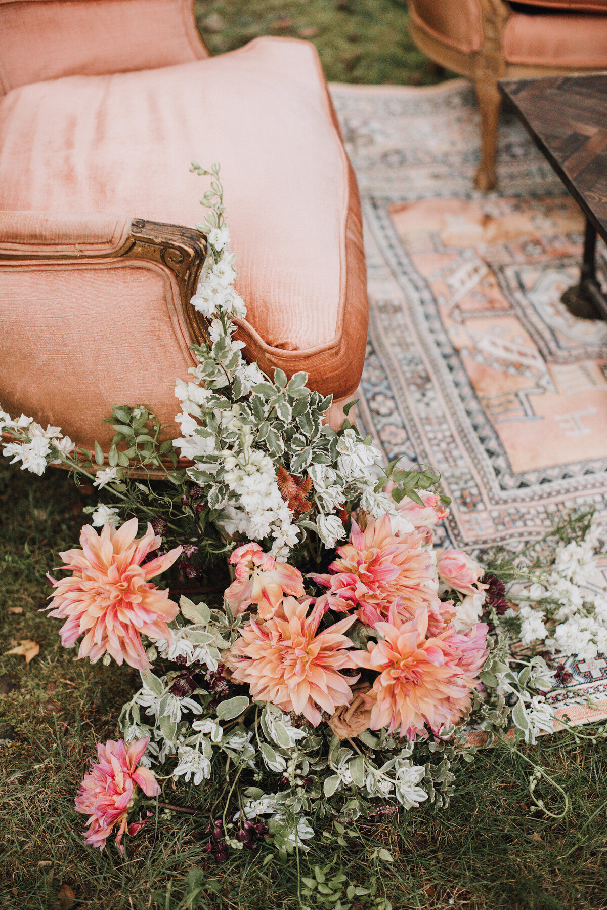 A poeach and ivory outdoor wedding lounge with a copper floral arrangement sitting on a tribal patterned rug