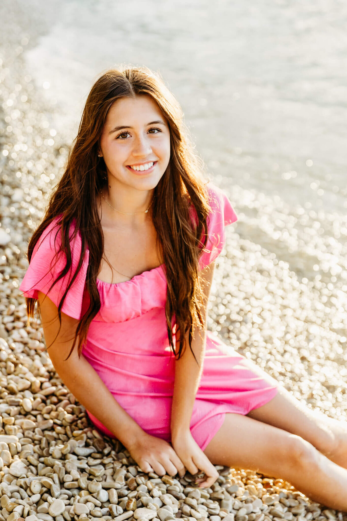 beautiful Appleton senior girl sitting on a beach in Door County and looking up and smiling for her senior portraits