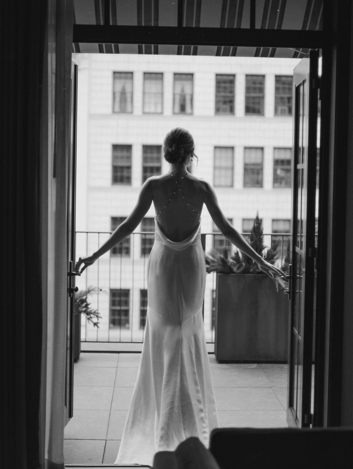 bride in backless pearl wedding dress opens doors onto balcony at Shinola Hotel