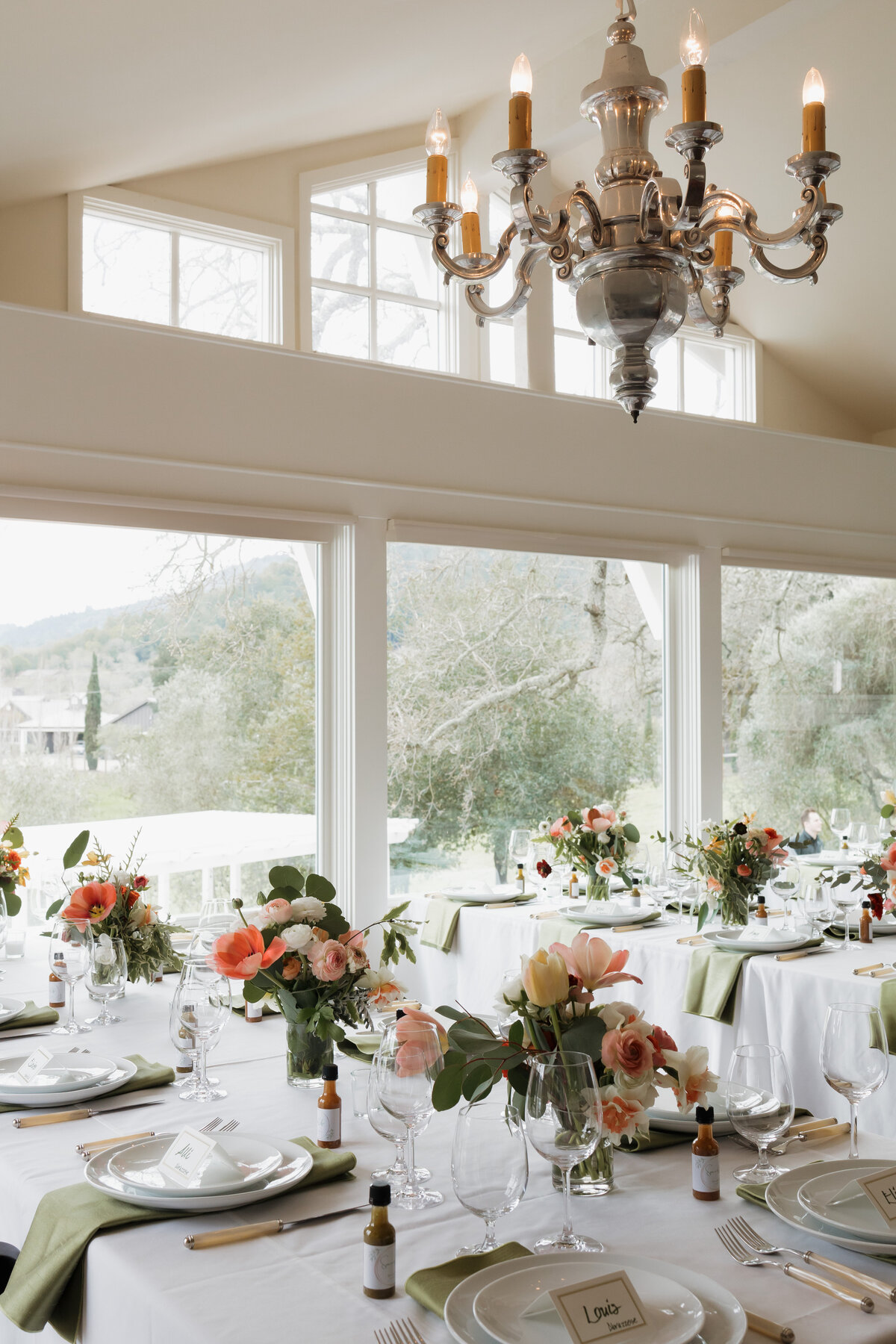 A beautifully decorated wedding reception table adorned with fresh flowers and soft candlelight, set against large windows with scenic views.