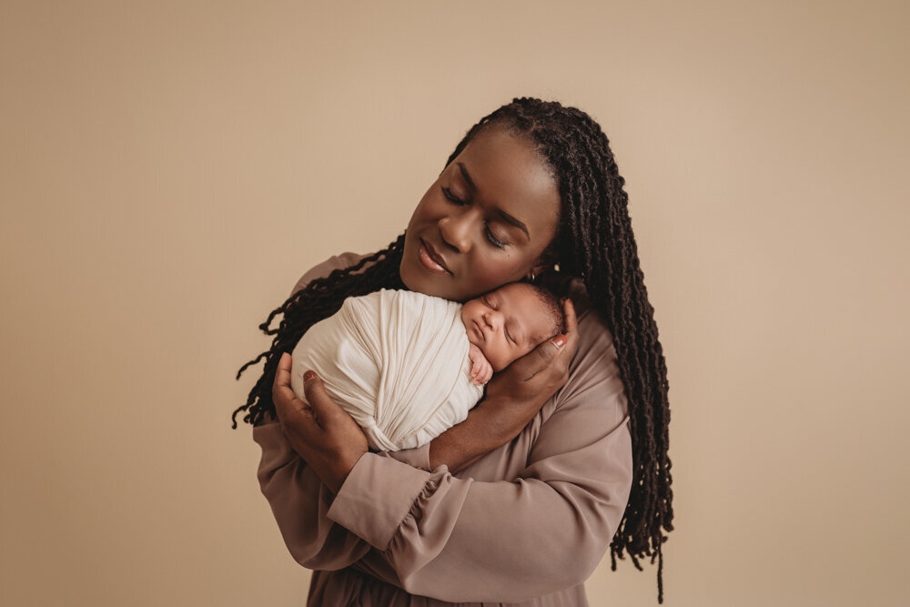 Newborn photos with Atlanta, Georgia newborn photographer of sleeping baby boy with hands under chin wrapped in cream swaddle being held by his mom