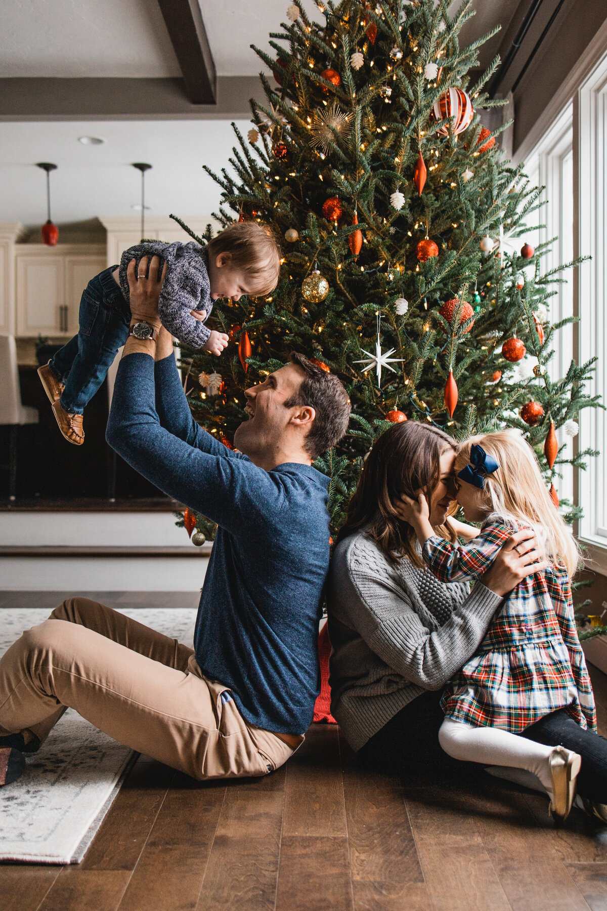 Mom and dad playing with kids in front of a Christmas tree