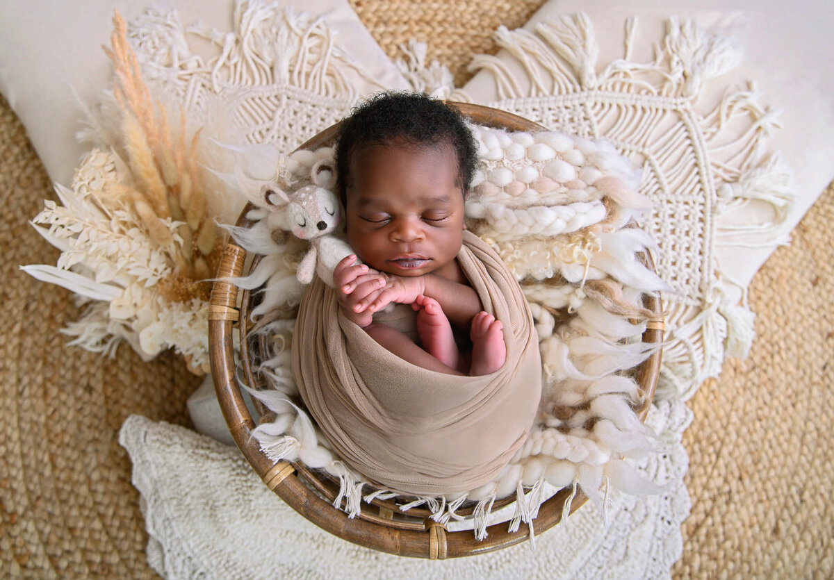 Newborn baby boy wrapped in beige on a boho style background for his newborn photography session in Burlington
