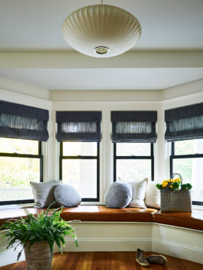 Interior decorators in Brookline, Boston, designed an original window seat with a leather cushion, linen Roman shades, and mid-century modern lighting.