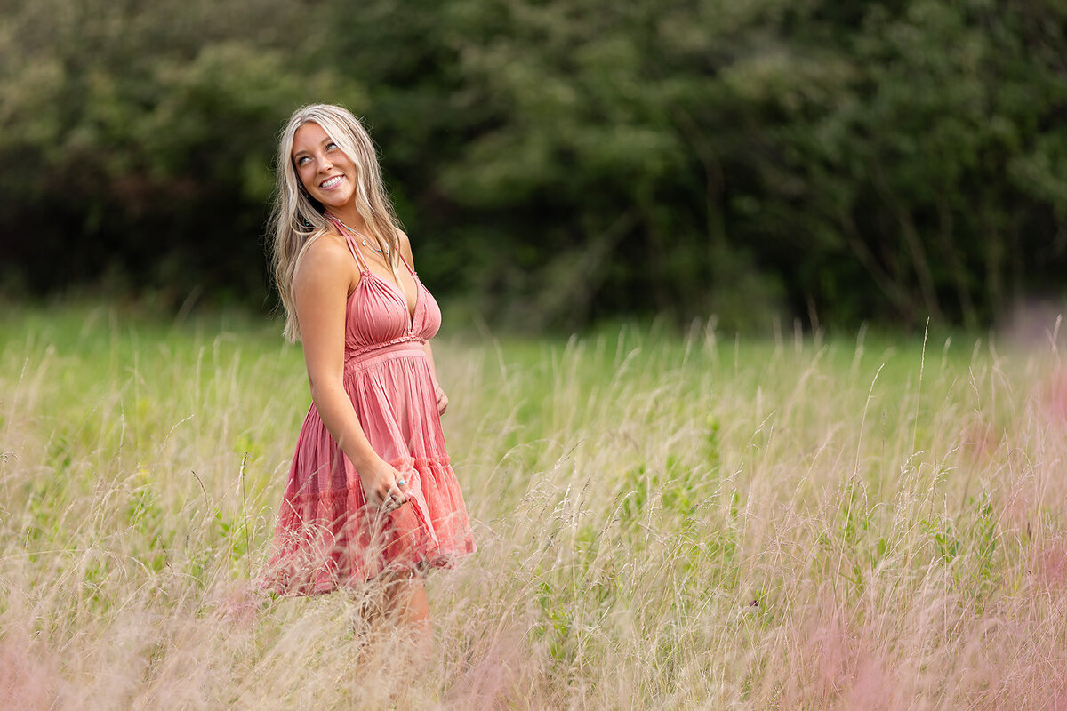 girl in field with pink flowers matching a pink dress looking behind her