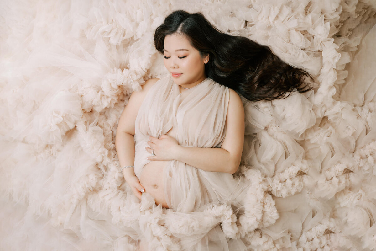 pregnant woman laying on ground with tulle spread out around her