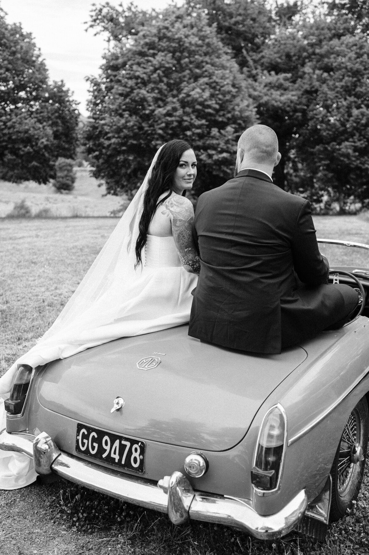 black and white photo of bride and groom on an old convertible MG at their christchurch wedding