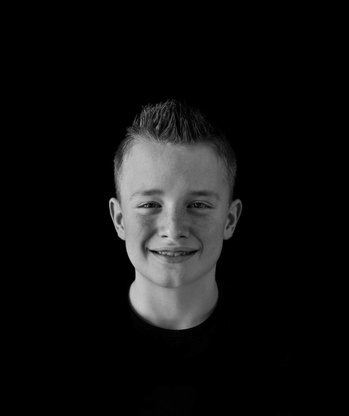 Een portretfoto van een jonge man met een open en vriendelijke uitstraling, gefotografeerd tegen een donkere achtergrond