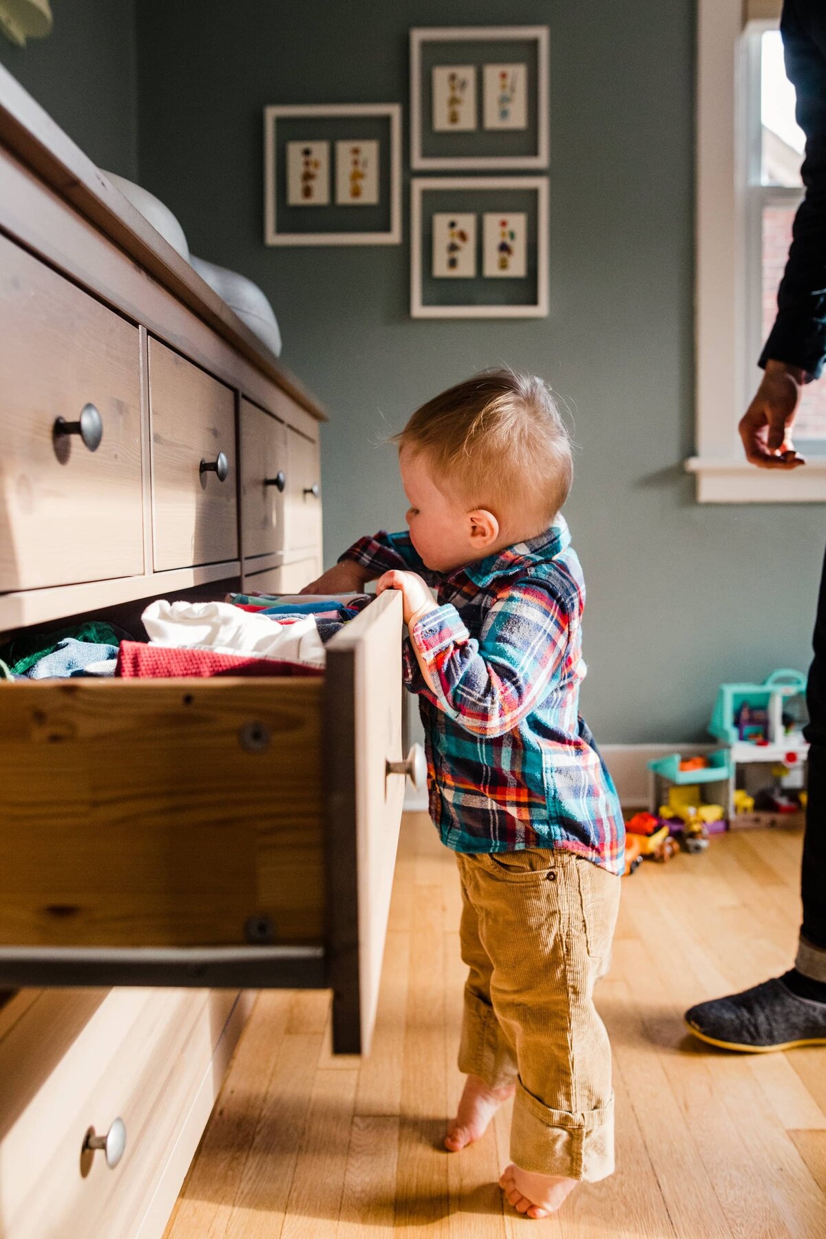 Toddler rummaging through an open drawer with toys scattered on the floor during a DIY family photos session.