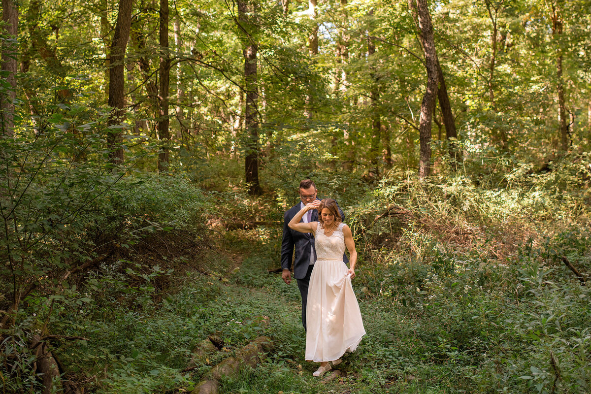 Bride leads groom on a walk through the woods.