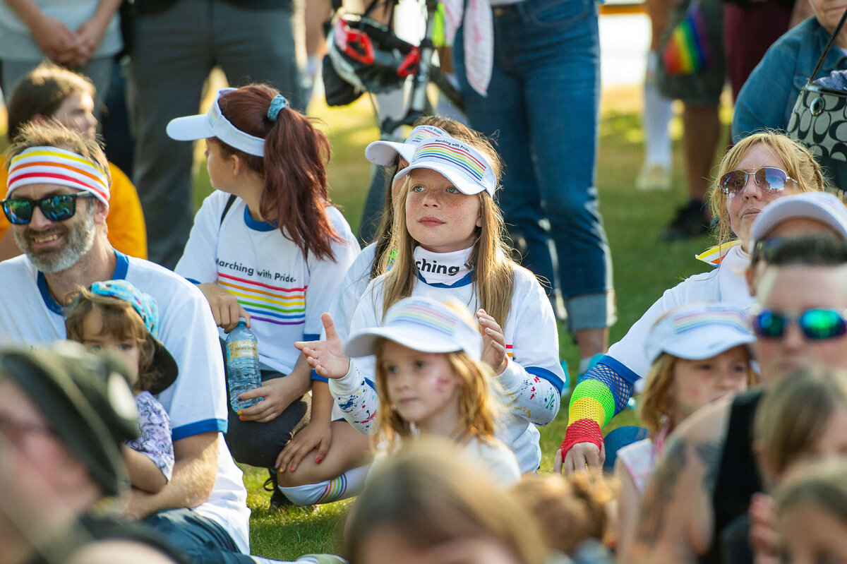 children wearing pride t-shirts and hats sitting on the grass watching the pride parade performers during the Tweed Canopy Growth pride parade.  Captured by Ottawa Event Photographer JEMMAN Photography COMMERCIAL