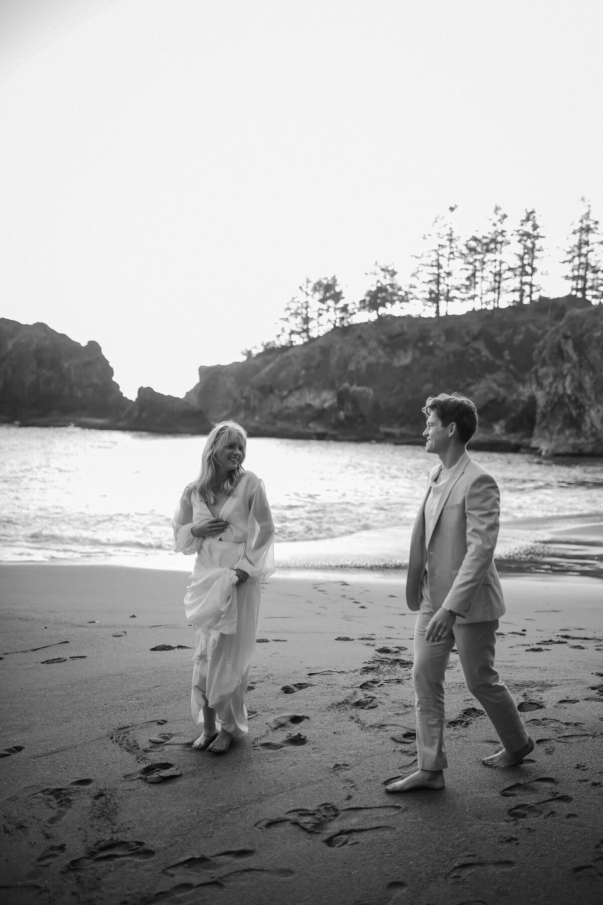 Black and white wedding photo with bride and groom laughing on the beach.