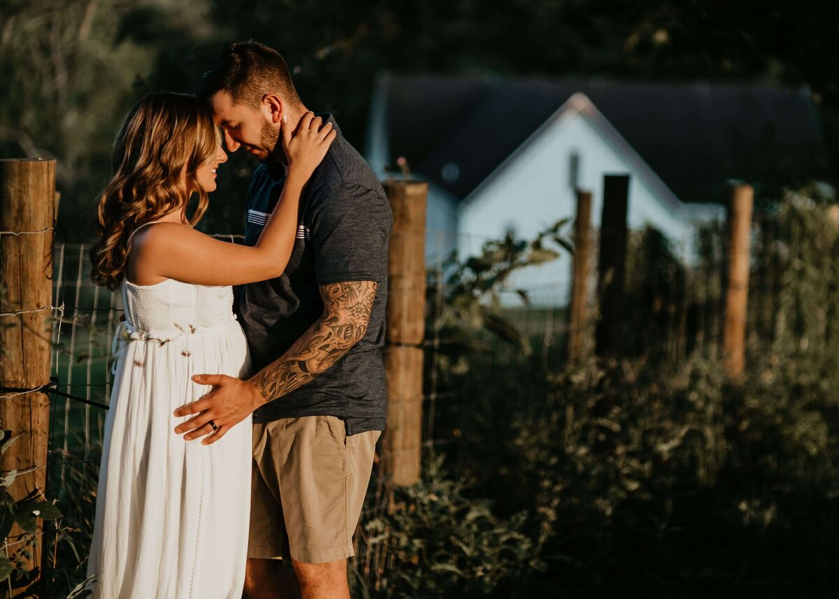 A couple embraces in front of a farmhouse during their maternity session with a Pittsburgh maternity photographer.