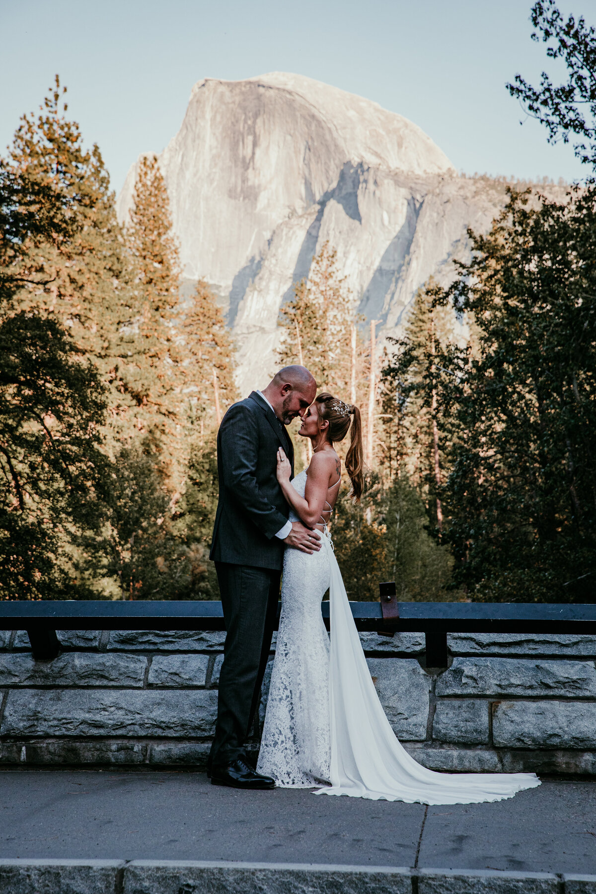 Bride and groom embracing at sunset with Half Dome towering in the background at Yosemite National Park.