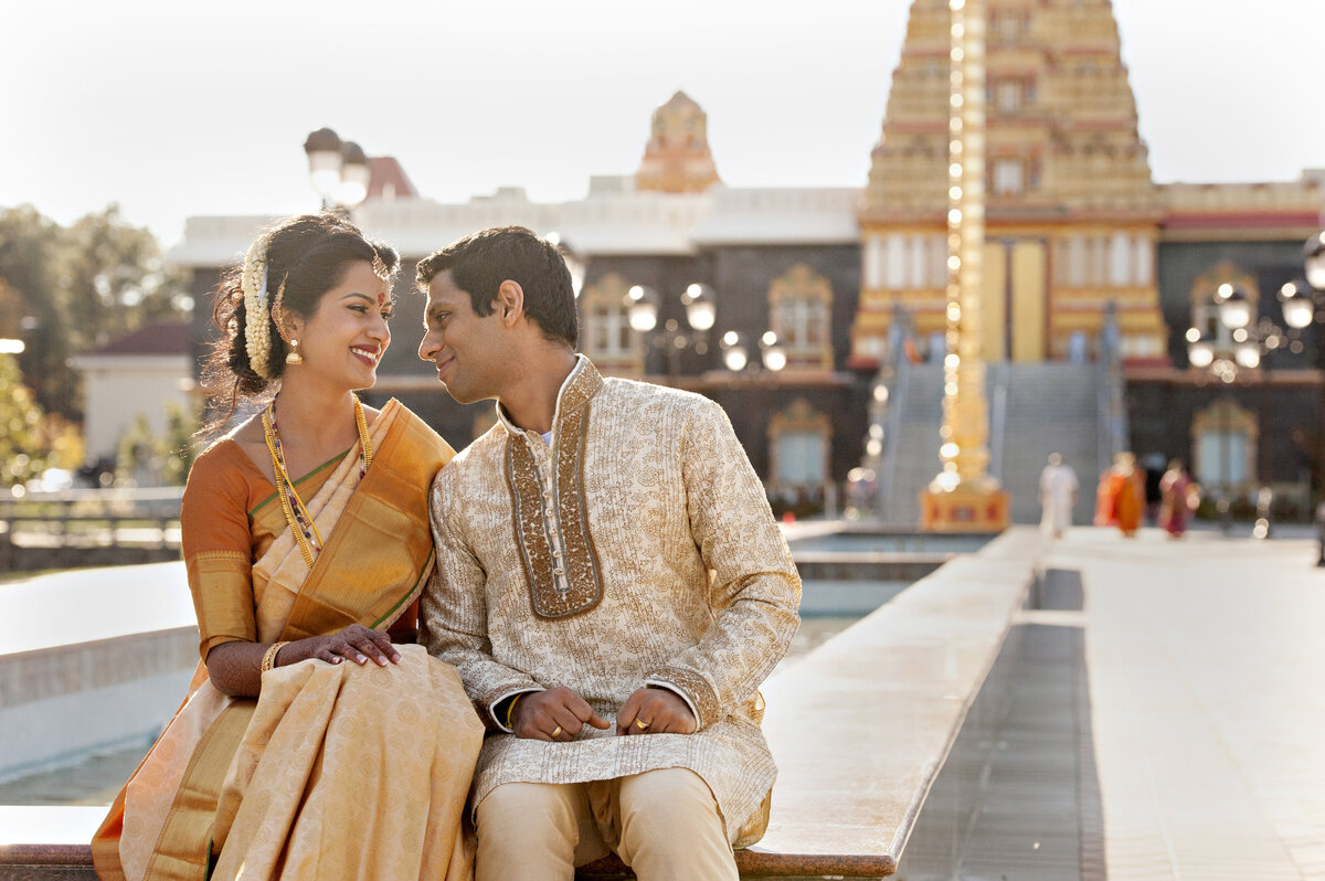 A couple in traditional Indian attire smiling at each other 
