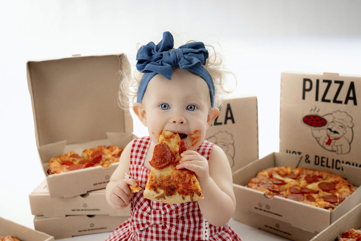 A young girl take a big bite of pizza for her Iowa Milestone Photos