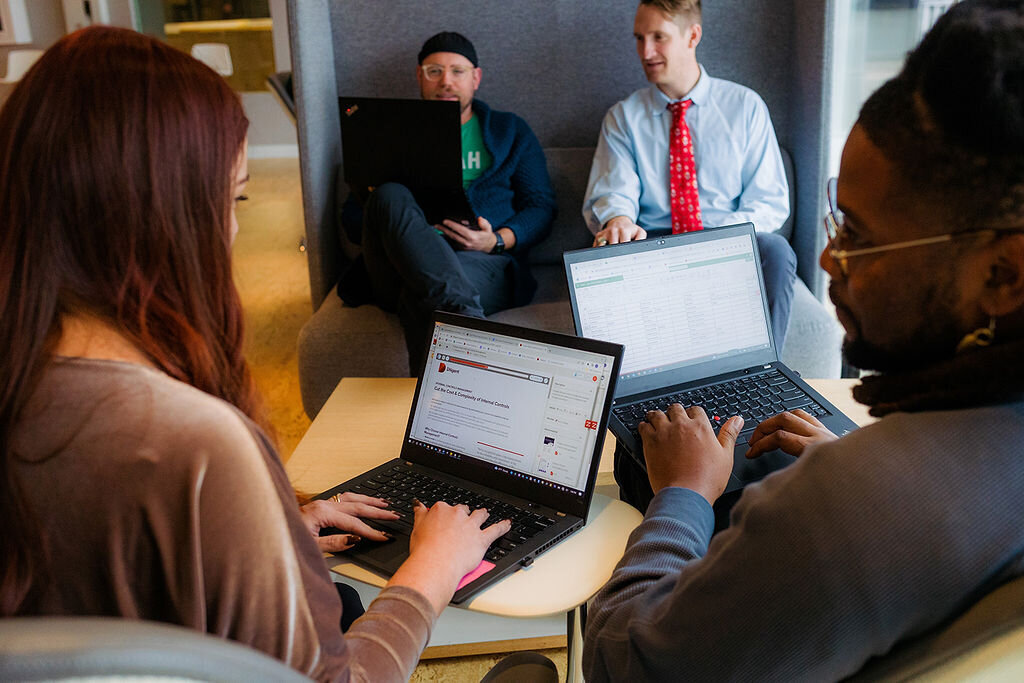 Two people type on laptops, while two other people work across the table from them.