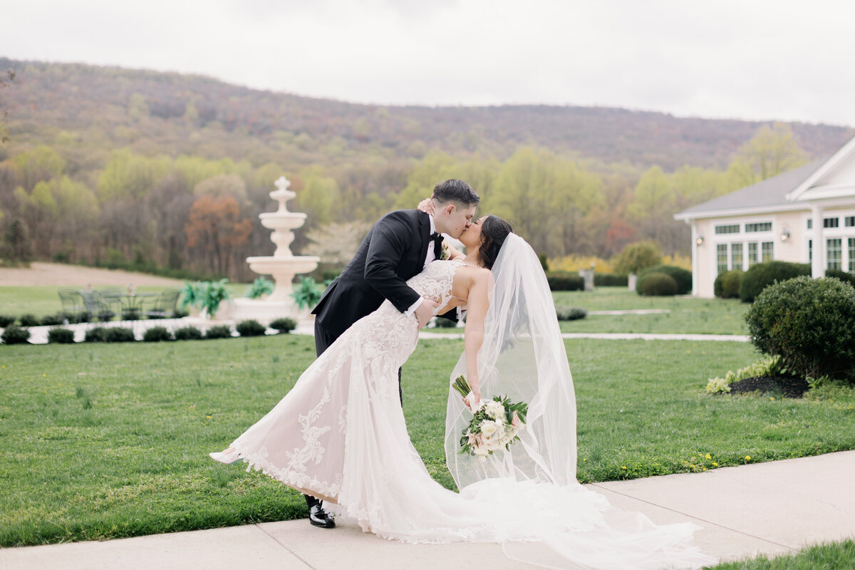 Bride and groom sharing kiss beside stone fountain during golden hour portraits at Springfield Manor.
