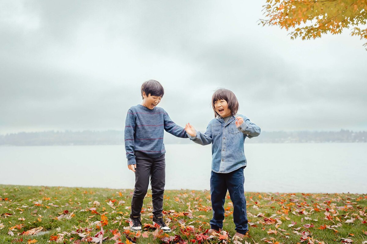 Candid photo of two brothers joyfully playing with autumn leaves in Kirkland, WA, full of laughter and seasonal color.