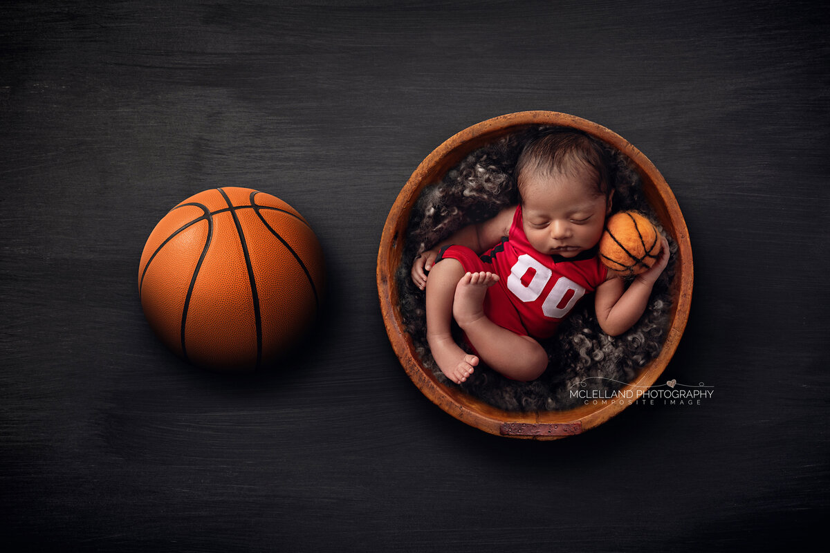 Newborn boy swaddled inside a basketball bowl for a sports-themed photo