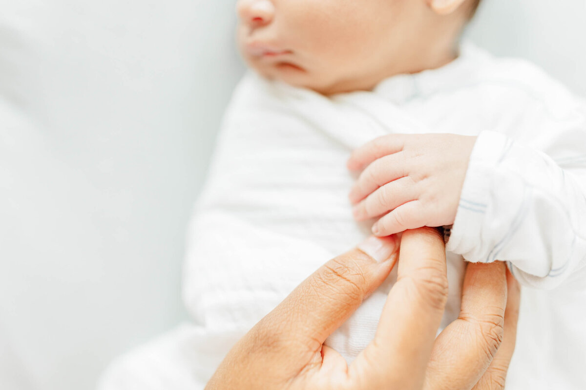 Closeup detail of newborn baby grasping his mother's hand