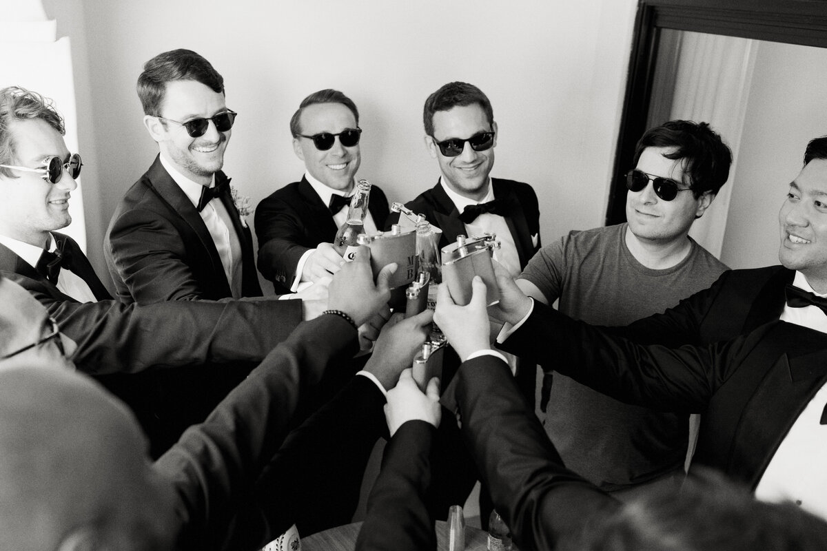 smiling groomsmen in tuxedos toasting with flasks