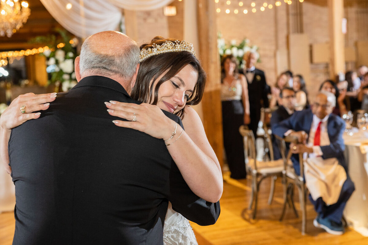 The bride is wearing a tiara and hugging her father