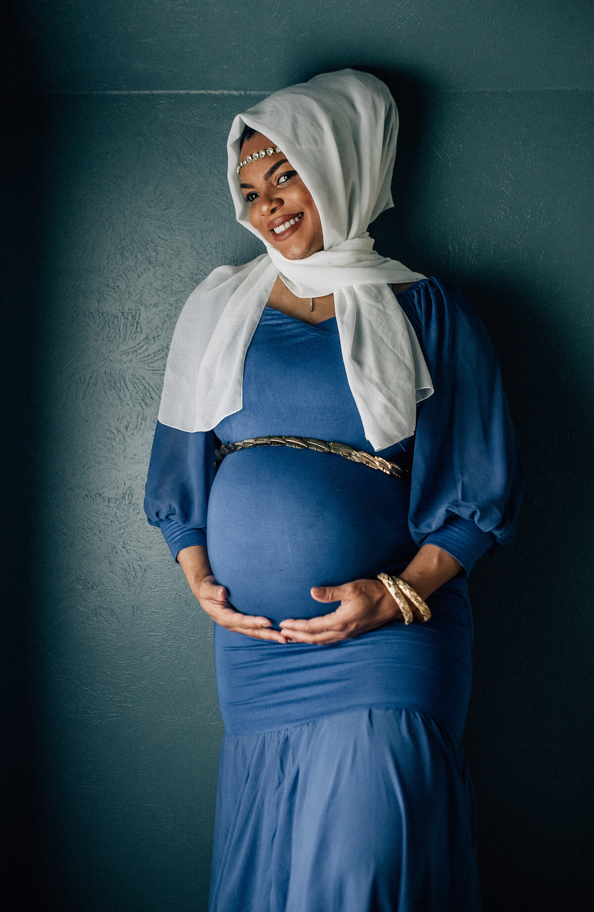 Pregnancy photoshoot with mom holding belly looking at camera.
