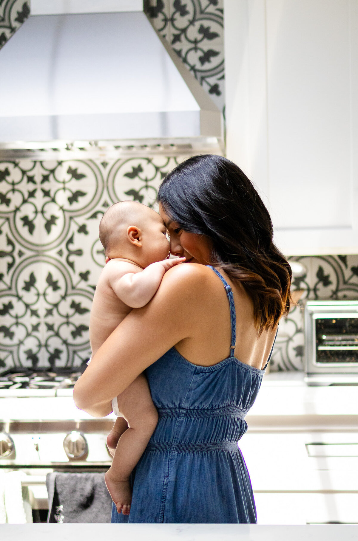 Mother lovingly embracing her baby in a kitchen with patterned tile, photographed by San Francisco newborn photographer.