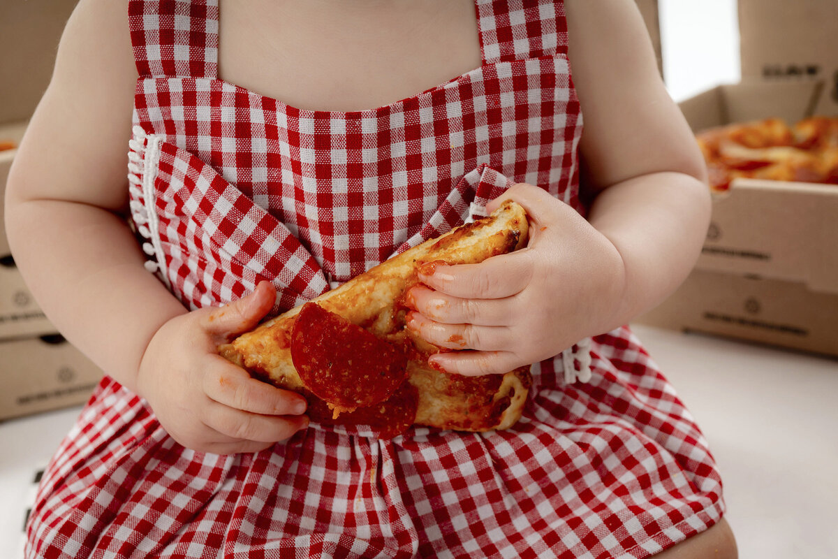 An Iowa Milestone Photographer captures a close up of a slice of pizza in a young girls hands