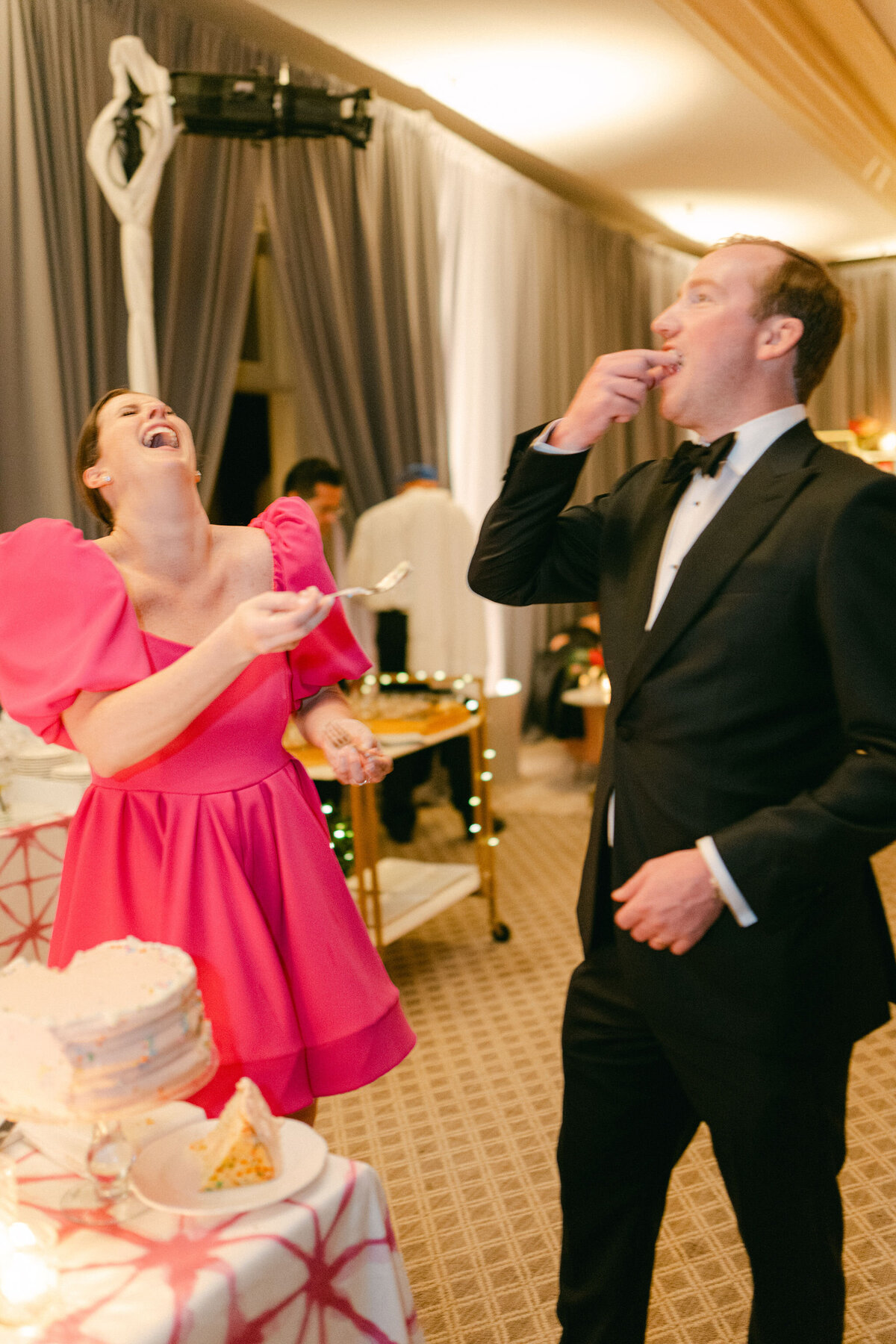 Bride and groom laughing while eating cake. 