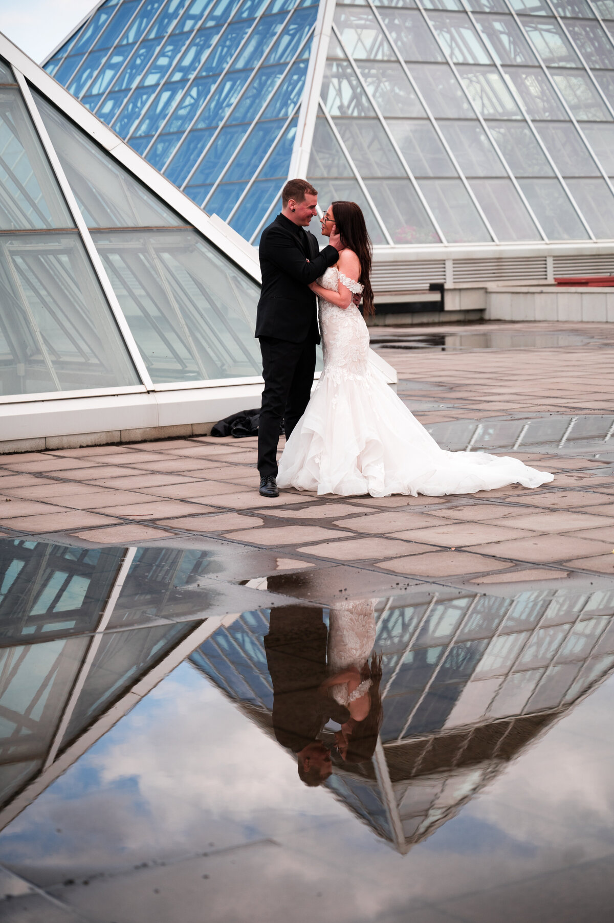wedding couple pose for photo with a reflection of them in a puddle