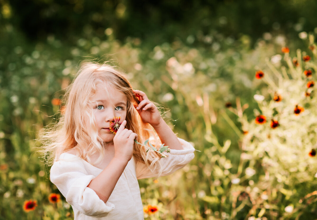 Little girl smelling wildflowers in a field.