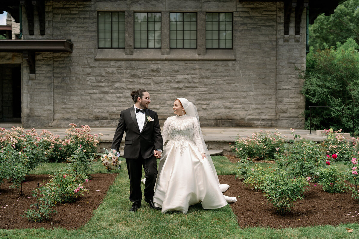 Bride standing in front of the historic stone architecture at Henry Ford Estate wearing an elegant long-sleeve wedding gown.