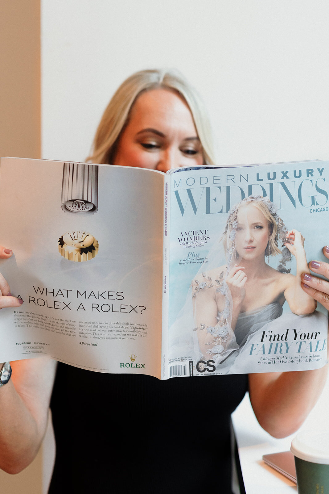 blonde woman is reading a wedding magazine and holding up to cover most of her face. You can only see her eyes reading the magazine.
