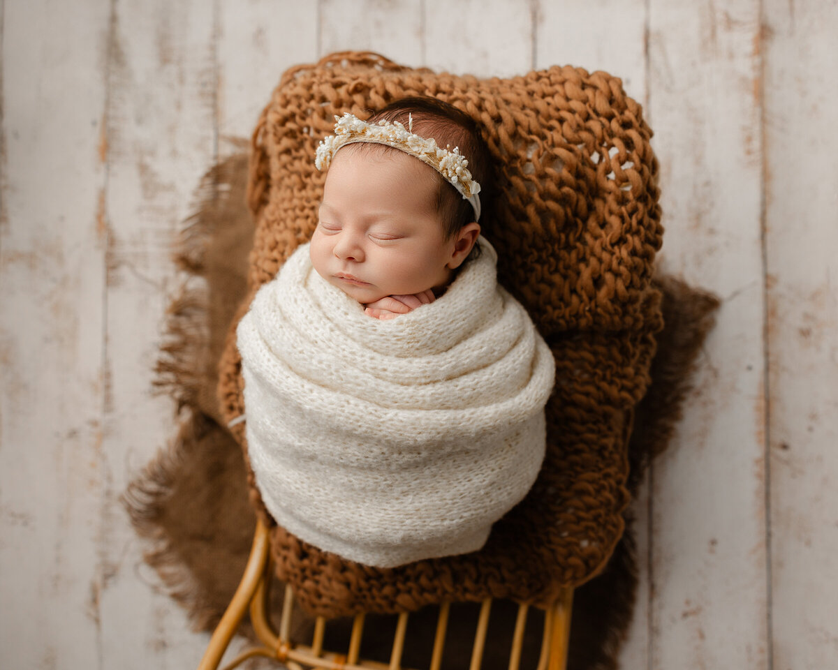 Newborn baby girl wrapped in a textured white knit swaddle, resting on warm brown layers during her in-studio Inland Empire session. Captured by Kaitlyn Dawn Photography.