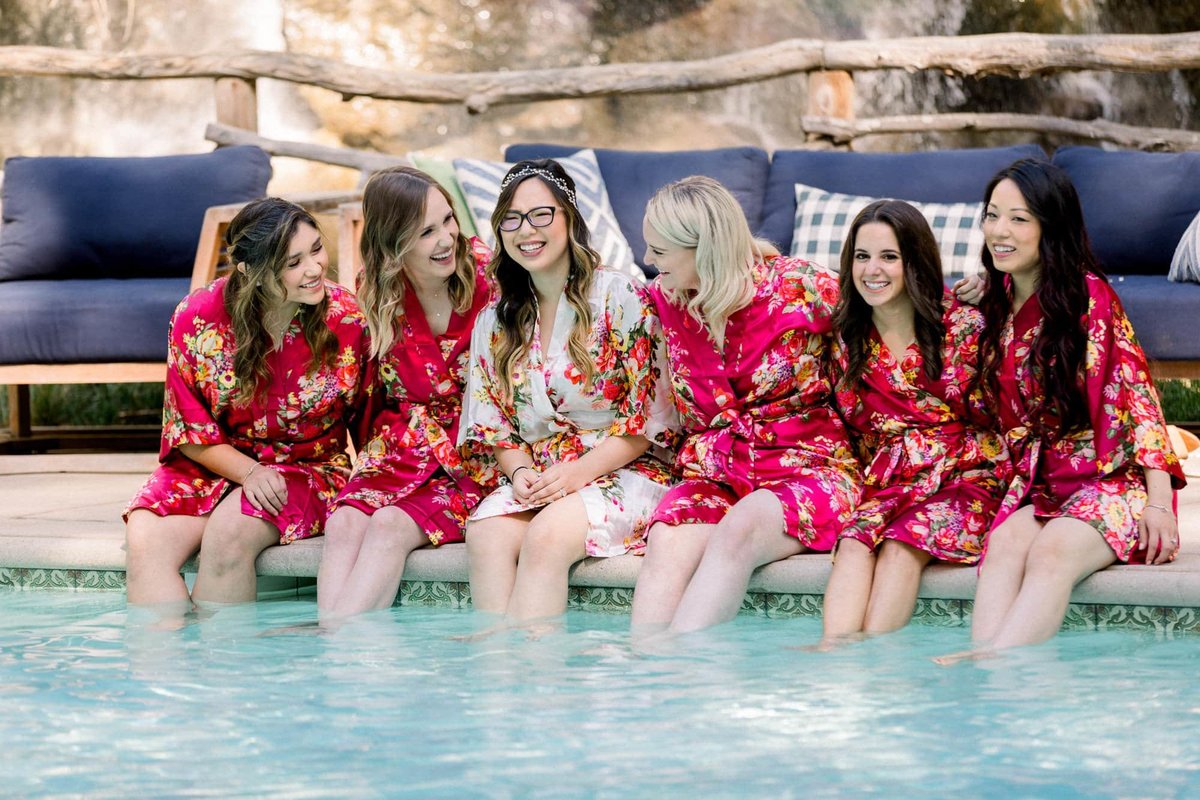 Bride and her Bridesmaids soak their feet and legs in the swimming pool while wearing their robes before getting ready for the ceremony